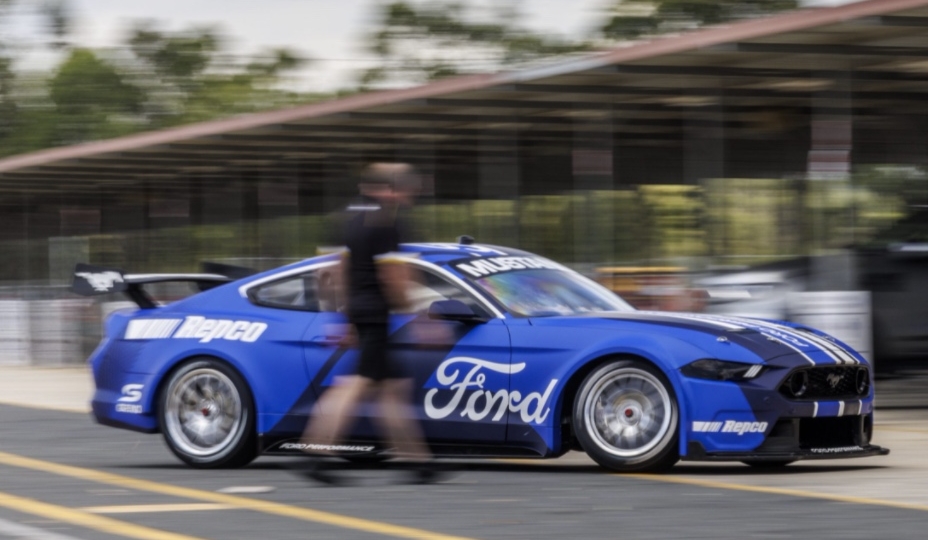 blue Ford race car speeding by a man shown as blurred
